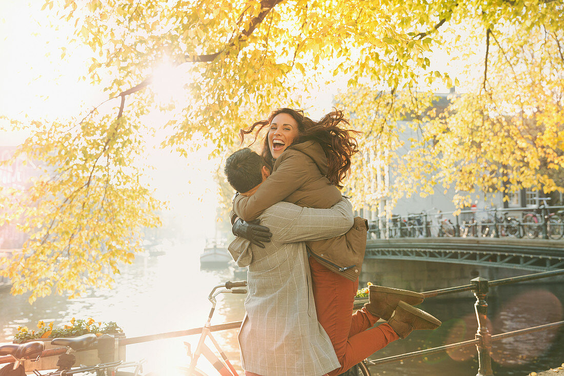 Enthusiastic couple hugging along autumn canal