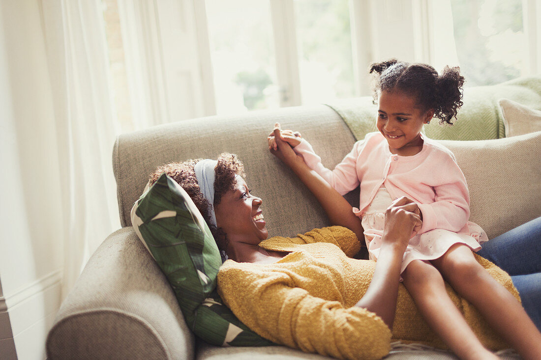 Playful mother and daughter holding hands on sofa