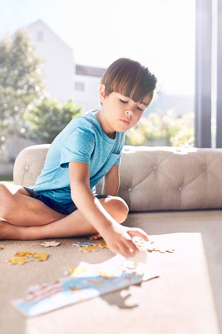 Focused boy assembling jigsaw puzzle on sofa
