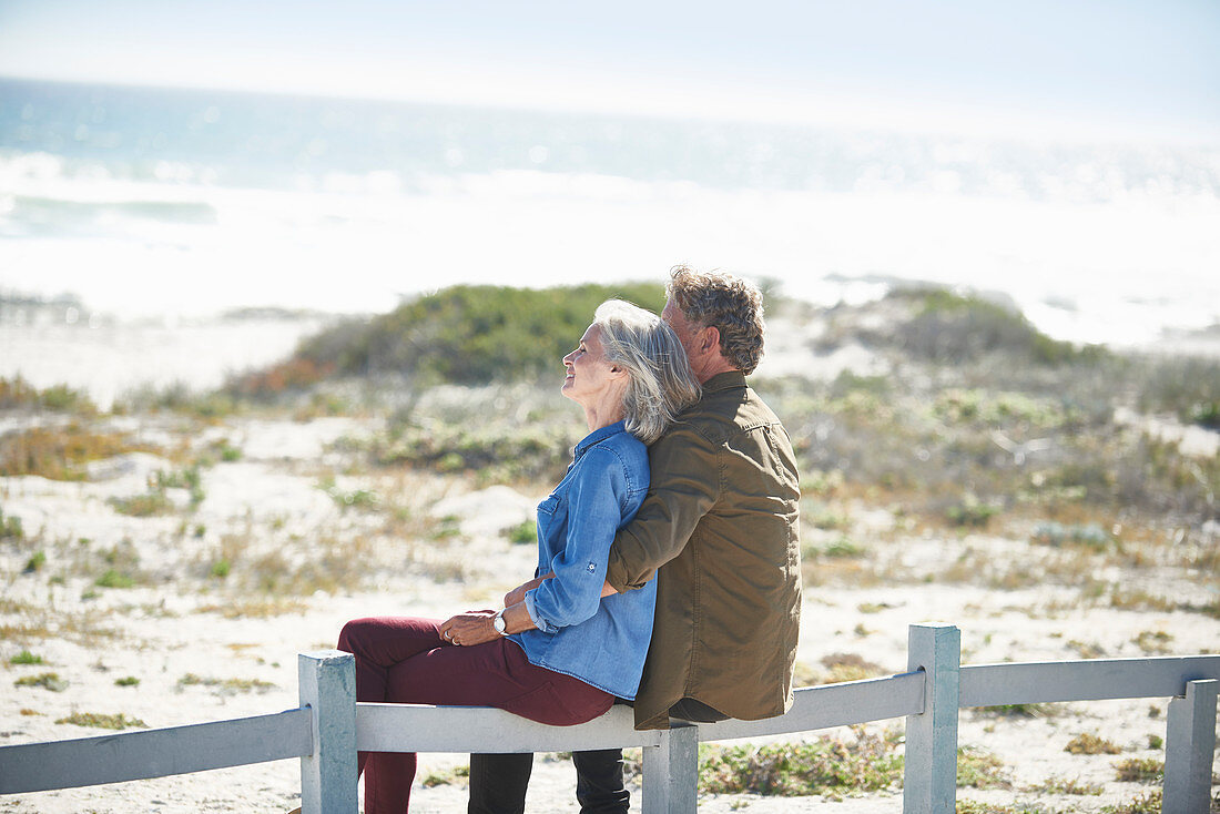 Affectionate senior couple sitting on beach fence