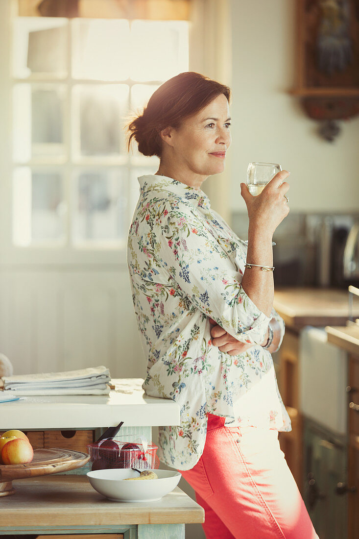 Pensive mature woman drinking wine in kitchen