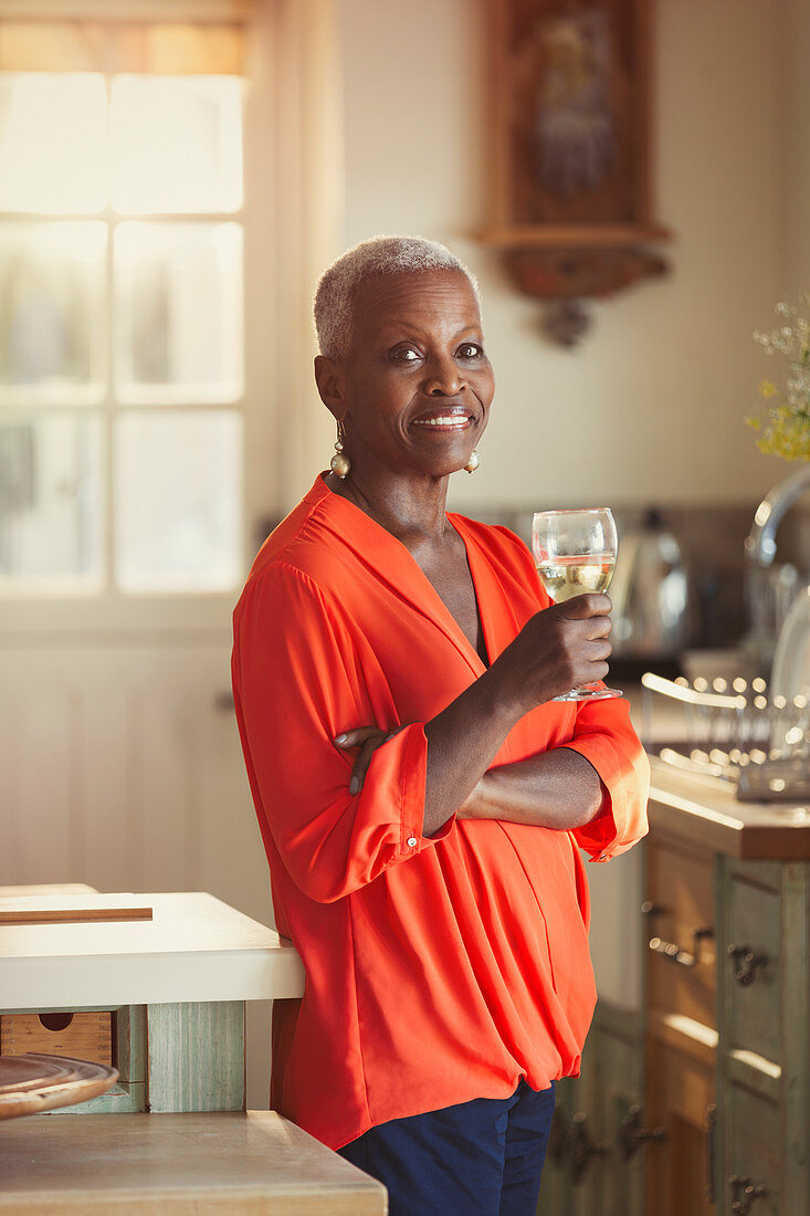 Portrait senior woman drinking wine in kitchen