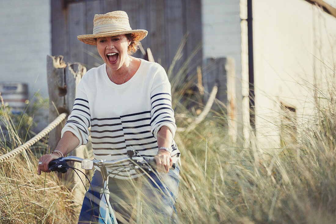 Mature woman riding bicycle on beach grass path