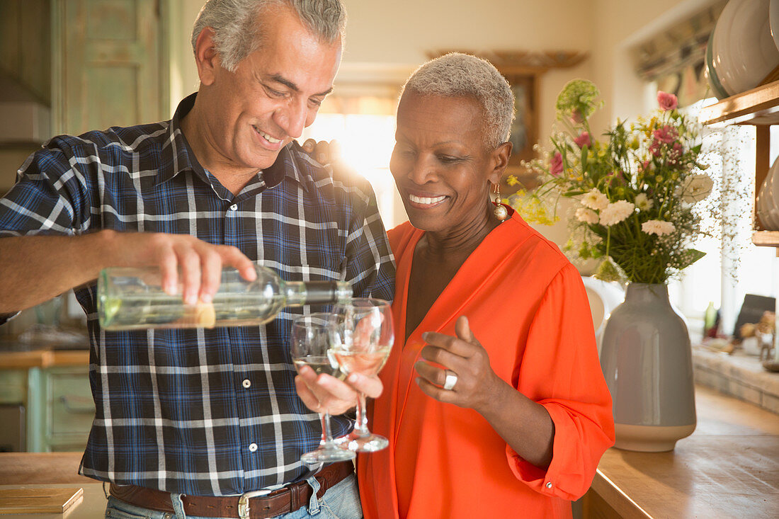 Senior couple pouring white wine in kitchen