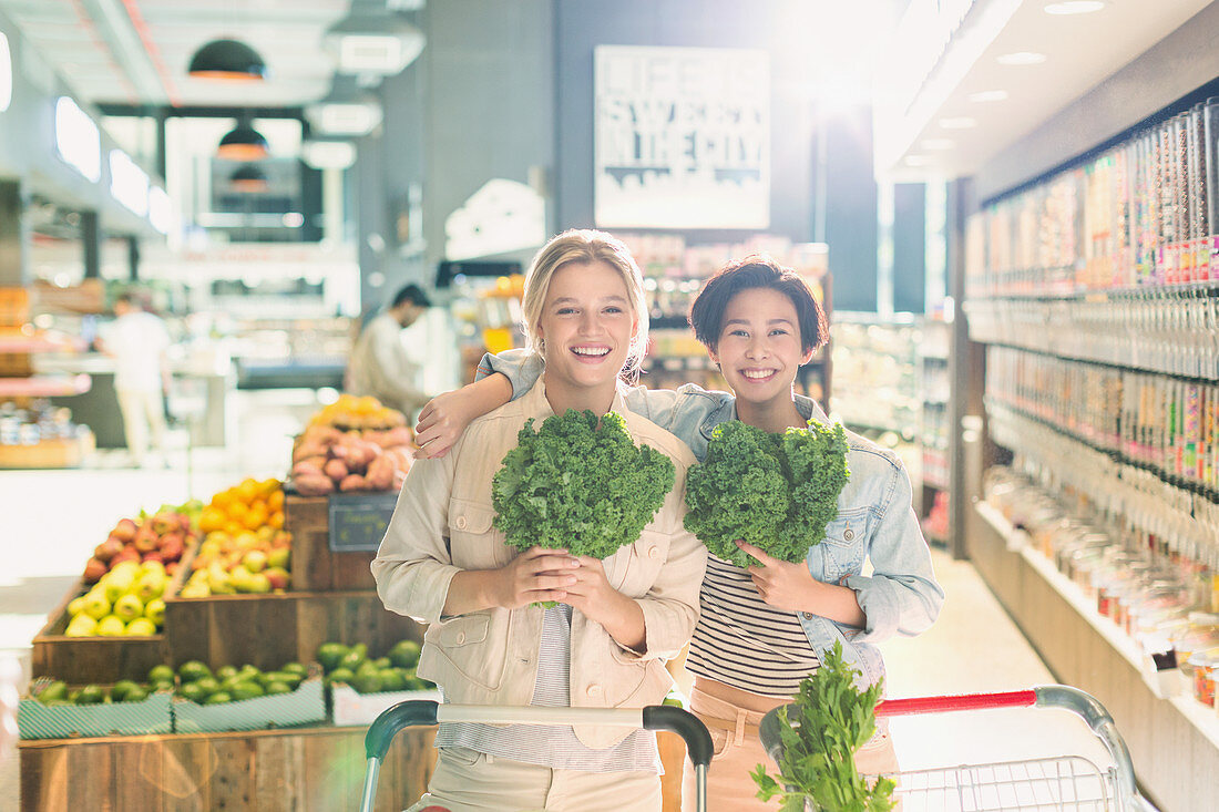 Portrait female friends holding kale in market