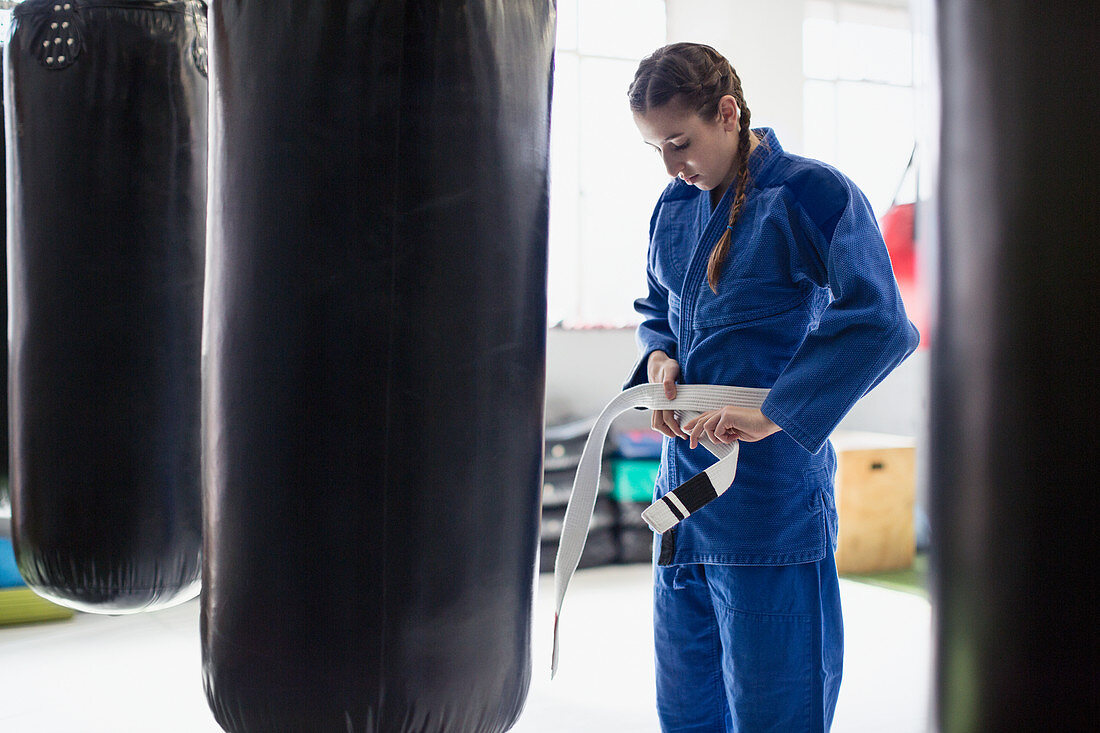 Young woman tying jiu-jitsu belt at punching bags