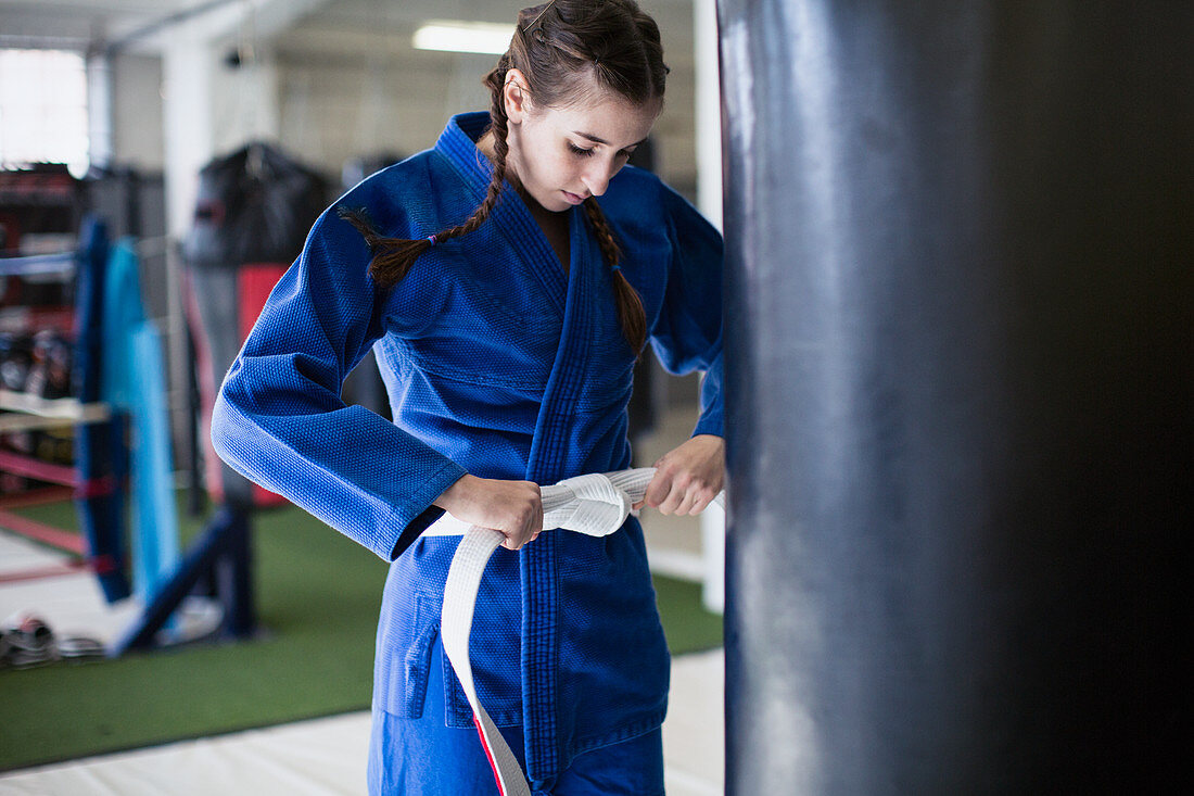 Young woman tightening jiu-jitsu belt at punching bag