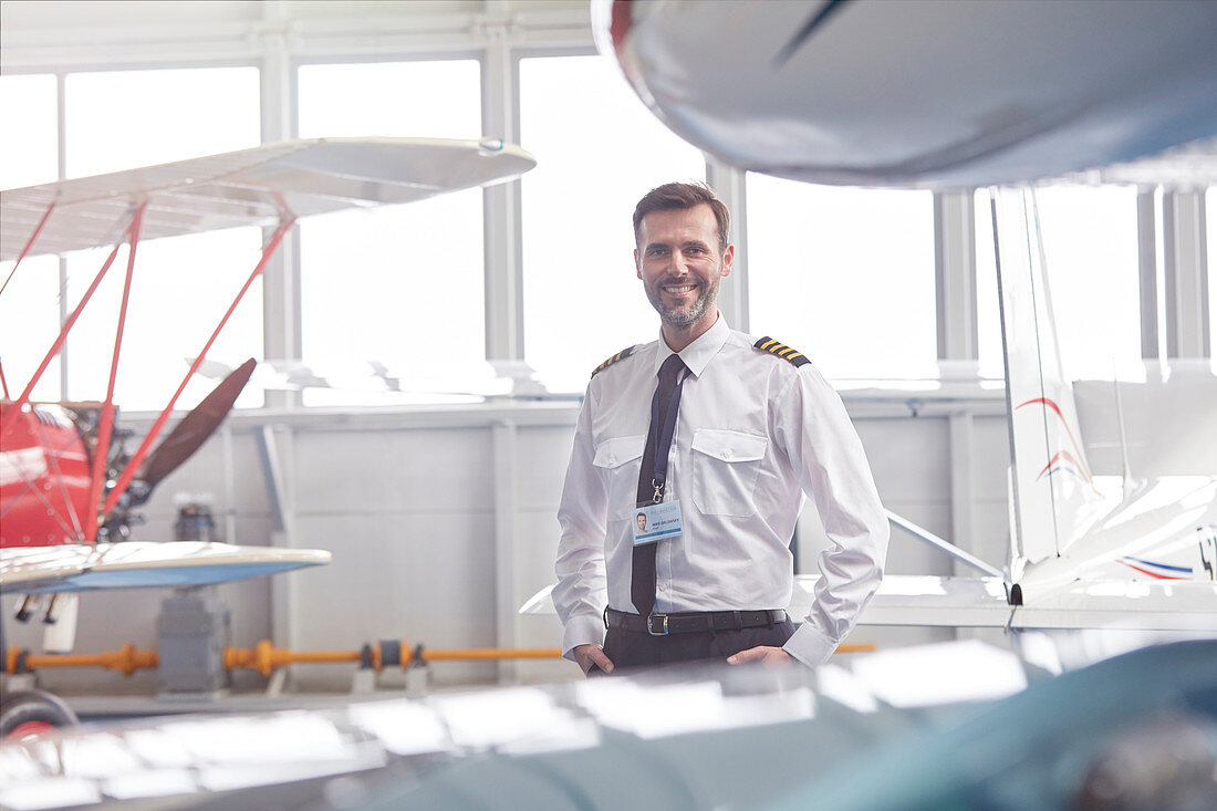 Portrait pilot standing near airplane in hangar