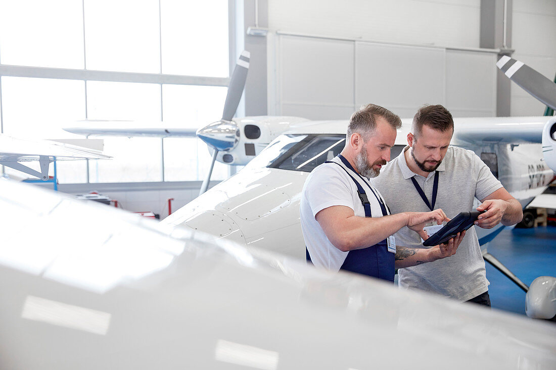 Male mechanic engineers using tablet near airplane