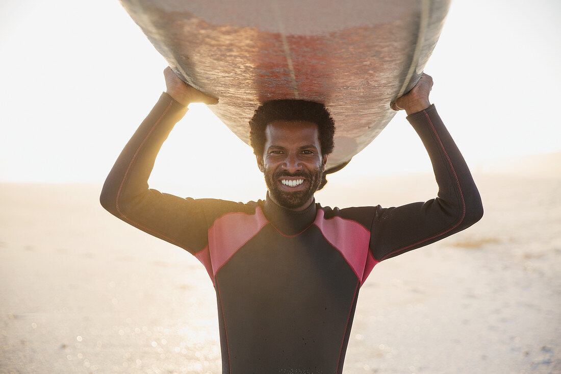 Portrait male surfer carrying surfboard overhead