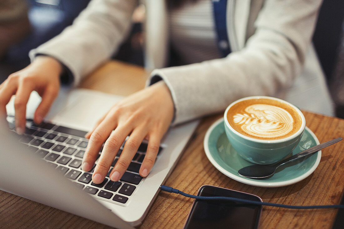 Hands of woman using laptop, drinking cappuccino