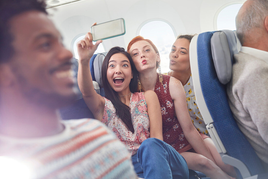 Playful friends taking selfie on airplane