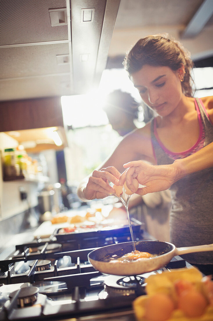 Young woman cracking egg over skillet on stove