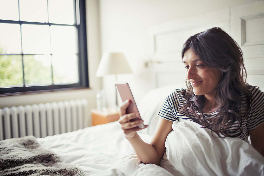 Young woman relaxing in bed, texting