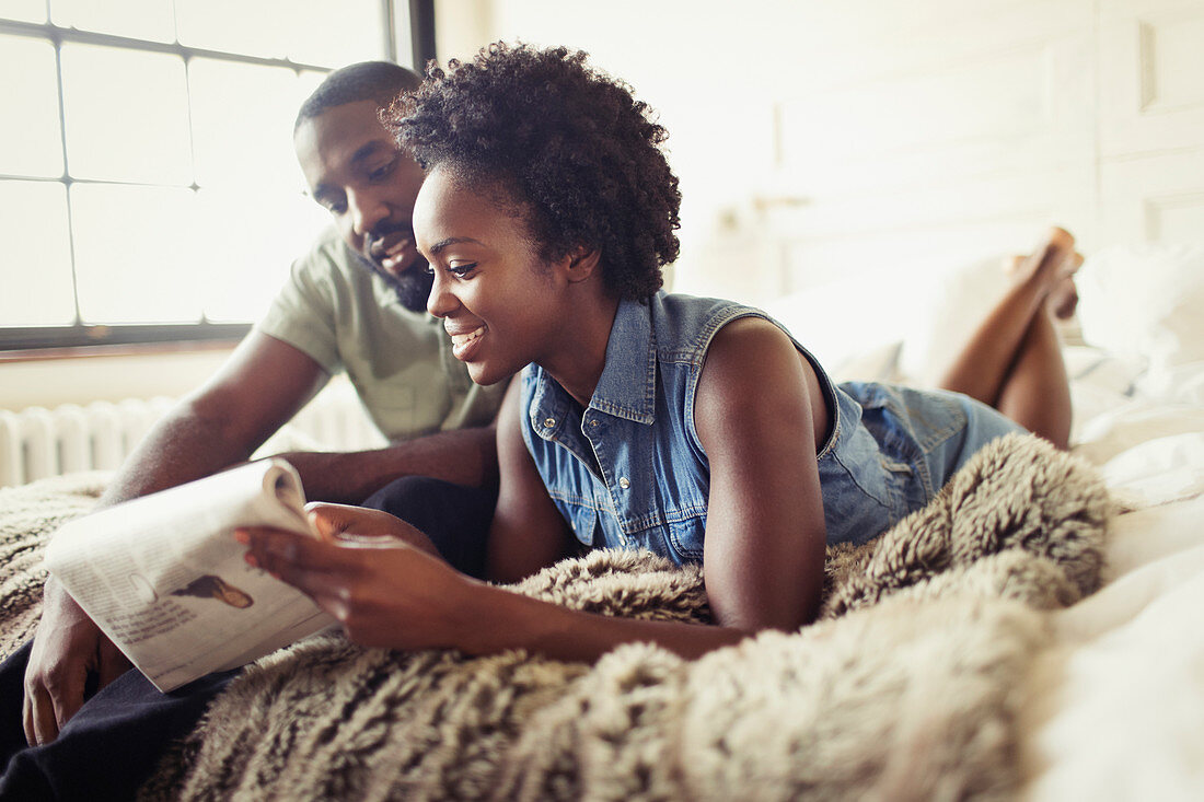 Couple relaxing, reading newspaper on bed