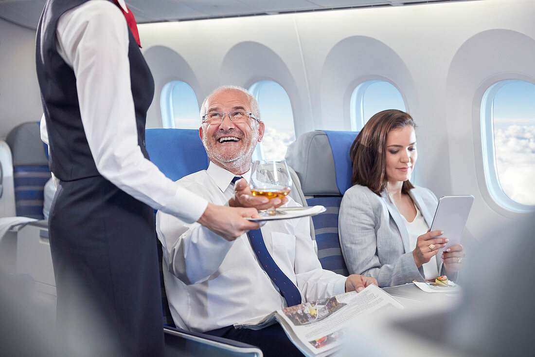 Flight attendant serving whiskey to businessman