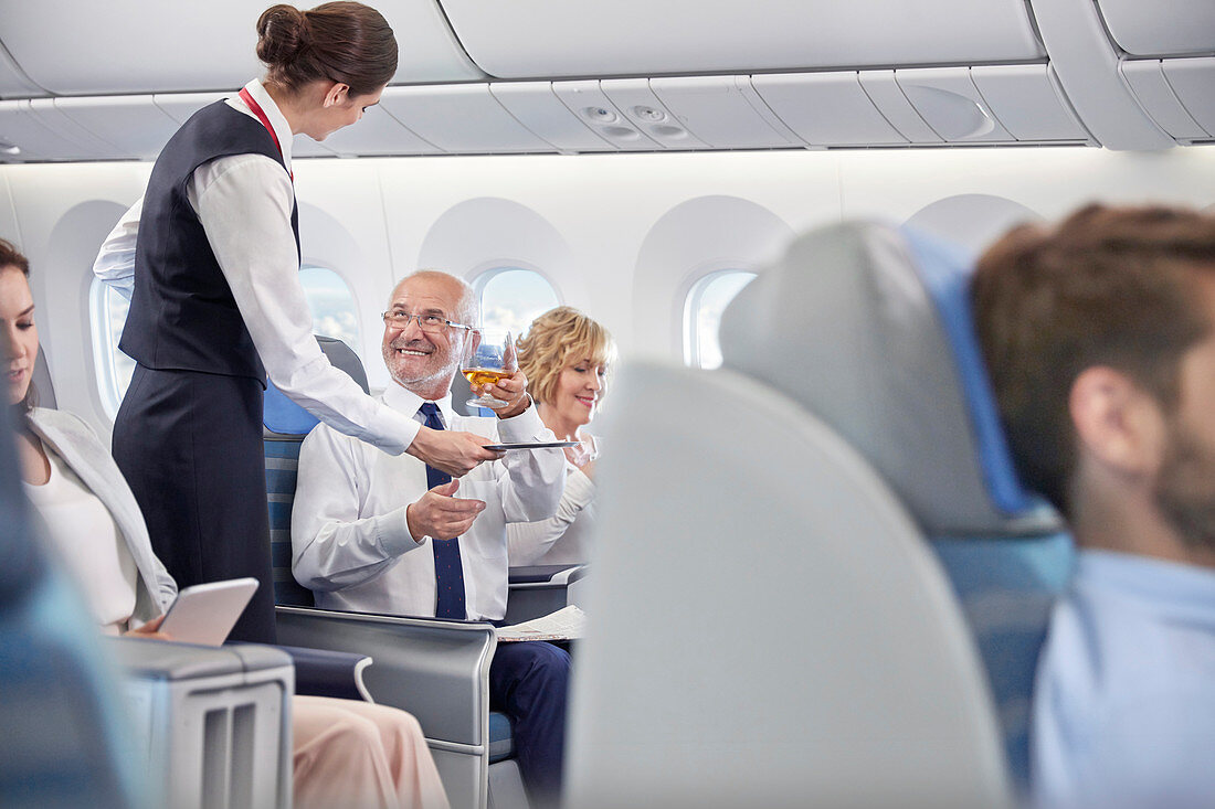 Flight attendant serving whiskey to businessman