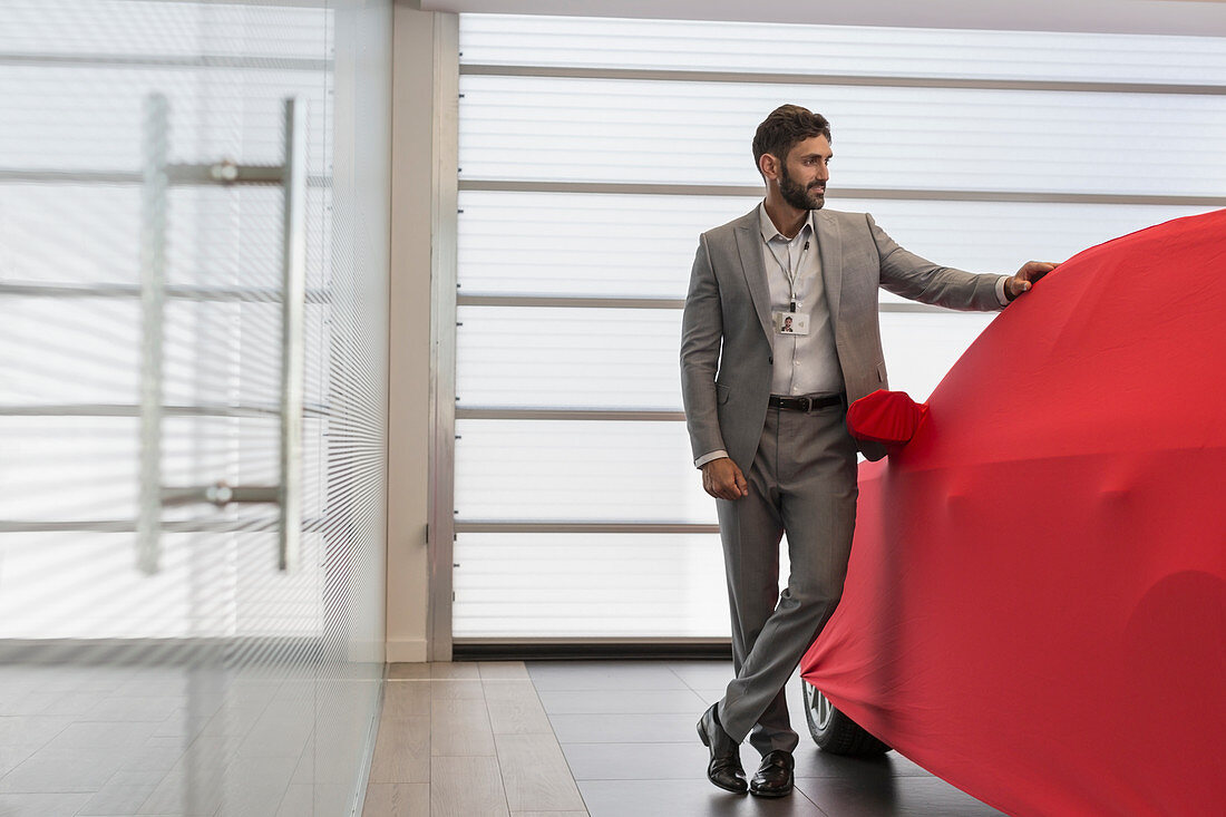 Car salesman standing at covered car in showroom