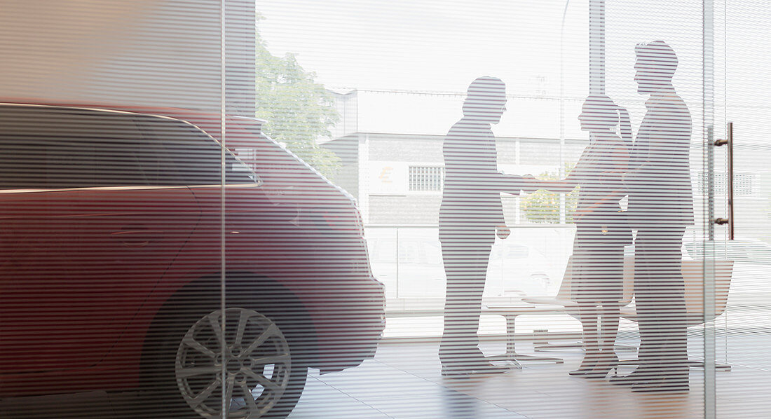 Car salesman shaking hands with couple customers