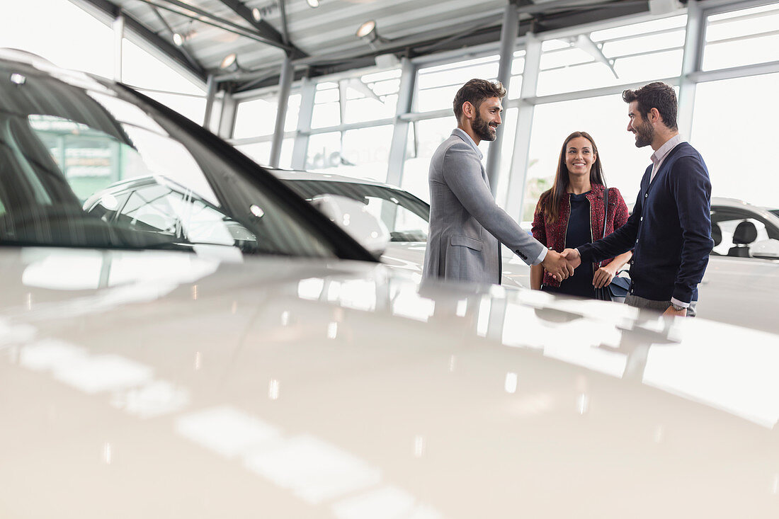 Car salesman shaking hands with couple customers