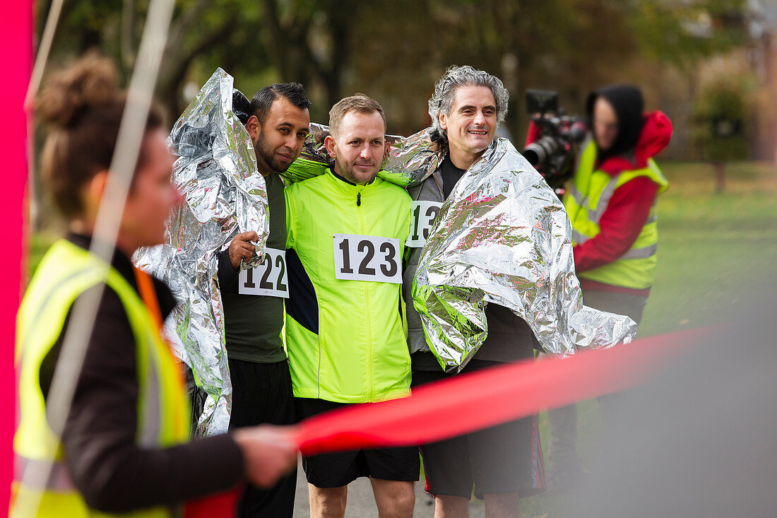 Male marathon runners wrapped in thermal blanket