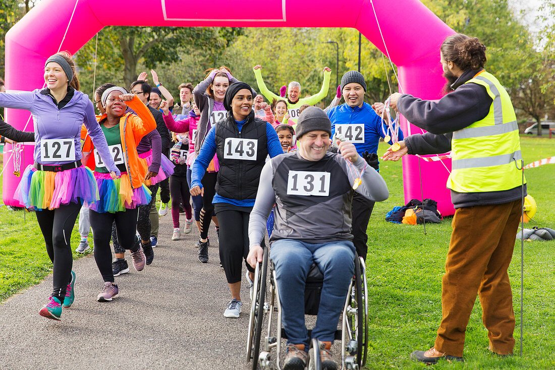 Man in wheelchair and runners receiving medals