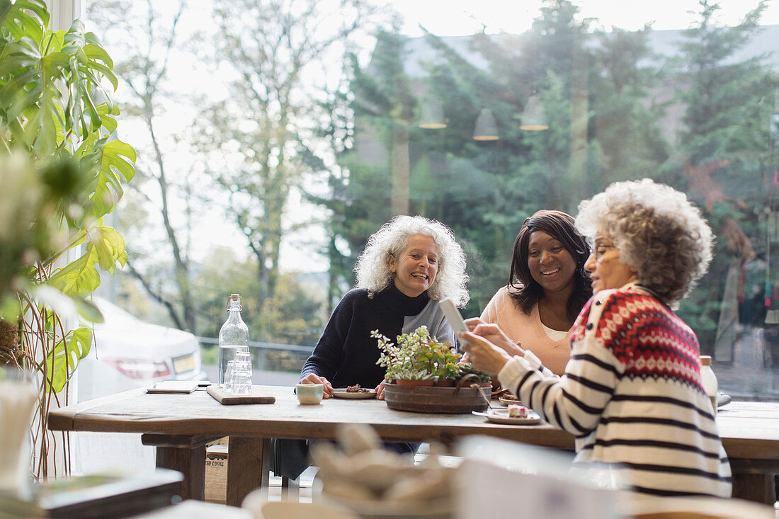 Smiling women friends using smart phone table