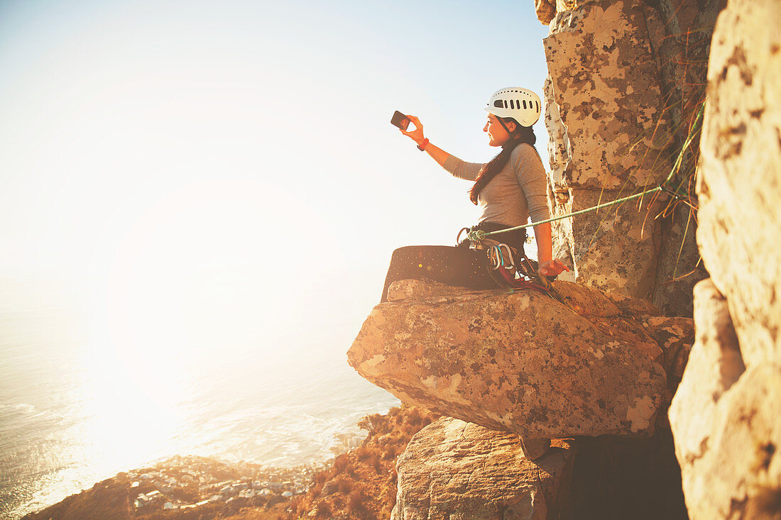 Female rock climber photographing sunny ocean view