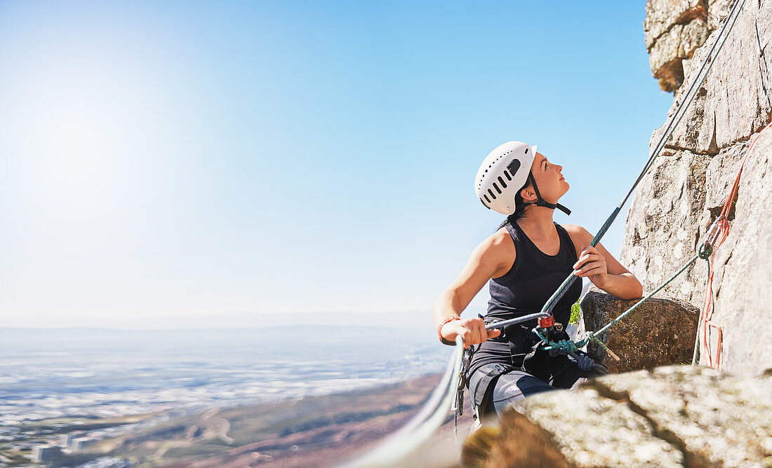 Female rock climber holding rope, looking up