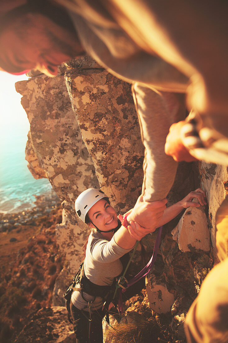Smiling female rock climber reaching for hand