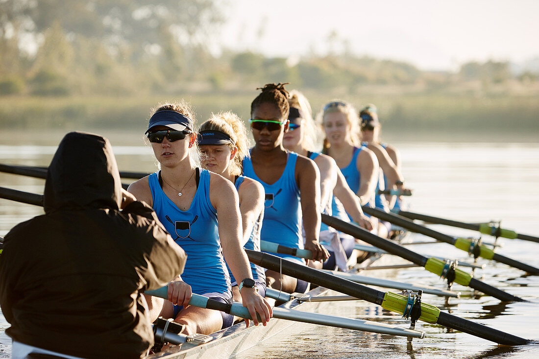 Female rowing team rowing scull on lake