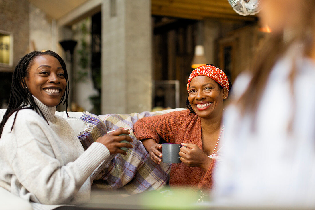 Smiling women talking and drinking coffee on sofa