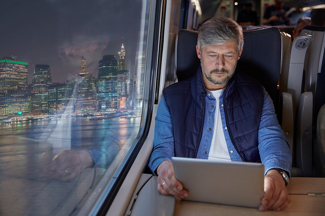 Man using digital tablet on train at night