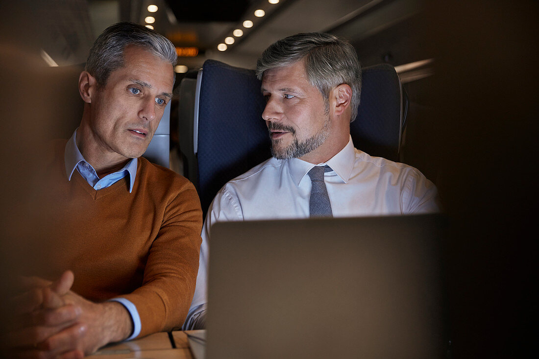 Businessmen talking, working at laptop on train