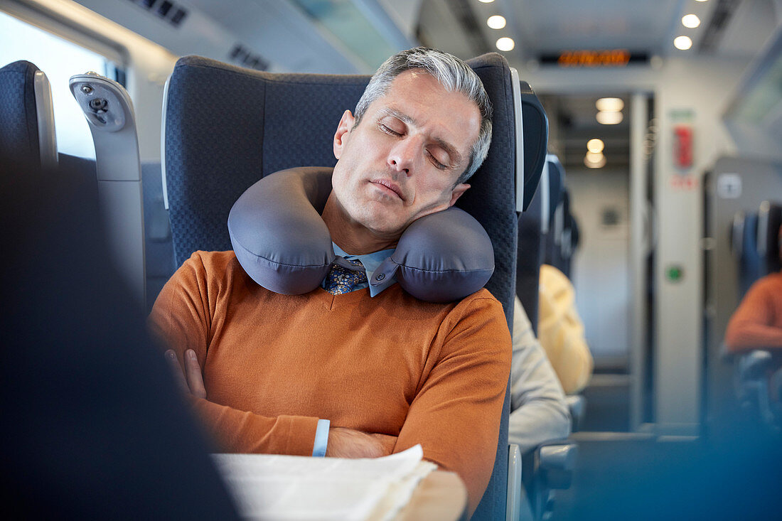 Tired businessman with neck pillow on train