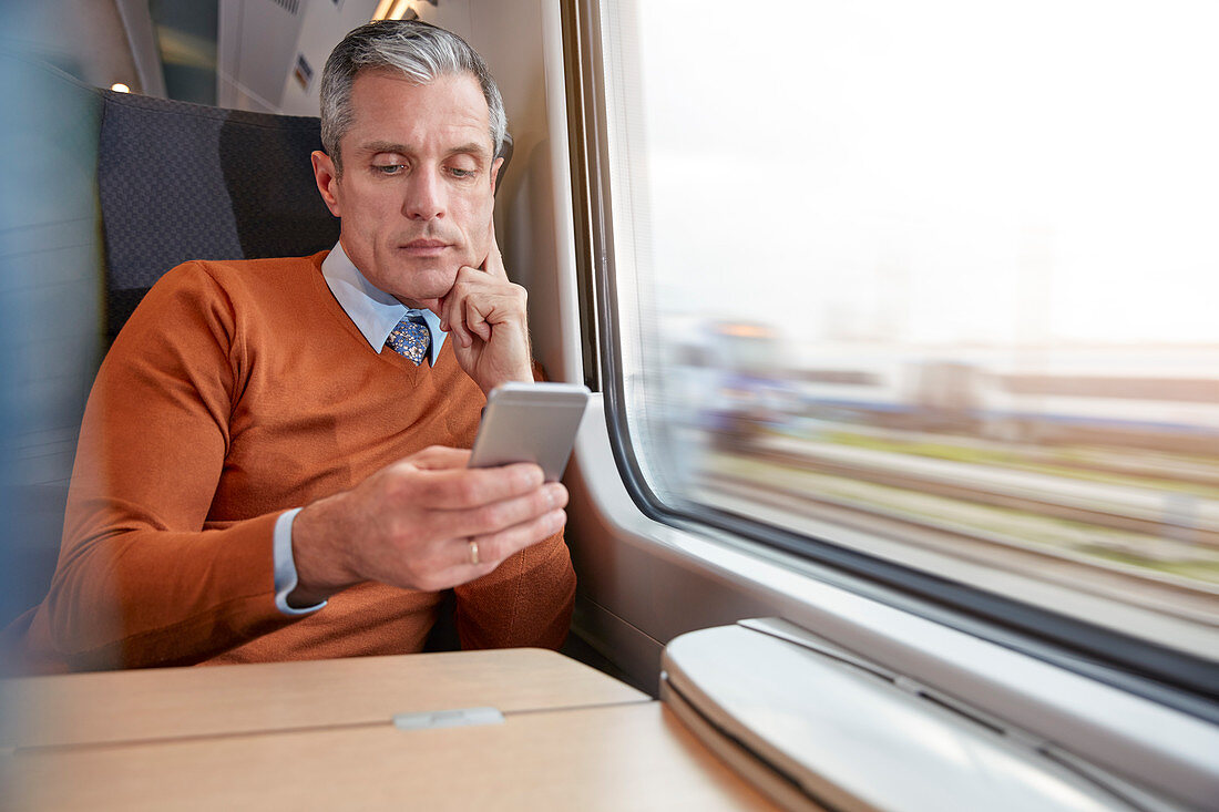 Businessman using smart phone at train window