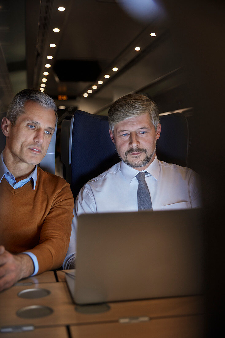Businessmen working at laptop on train at night