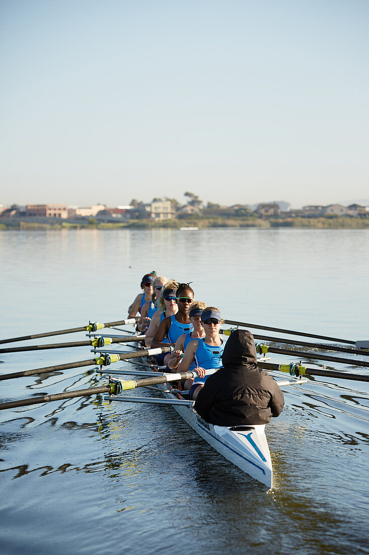 Female rowers rowing scull on sunny lake