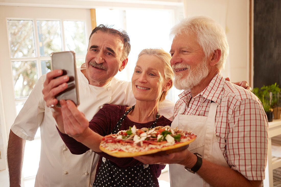 Chef and senior couple taking selfie with pizza