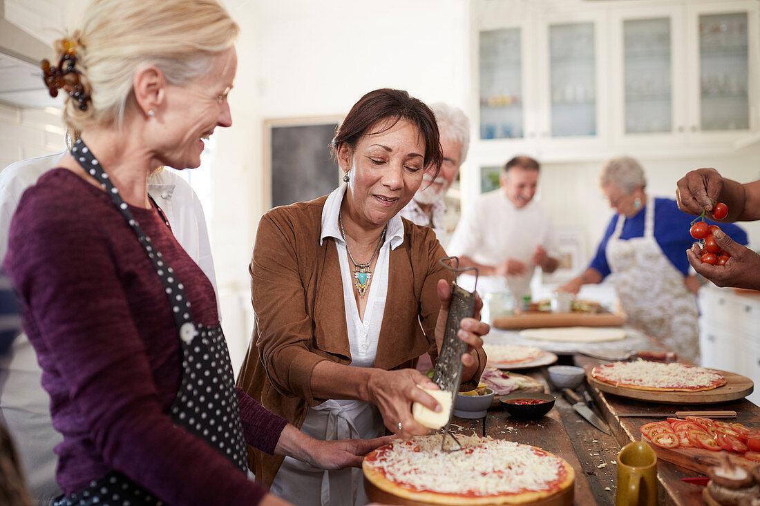 Senior women friends grating cheese over pizza