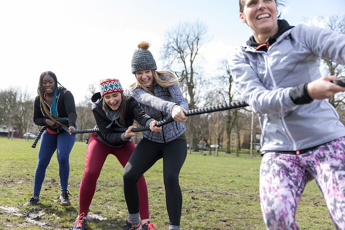 Determined women pulling rope in tug-of-war in sunny park