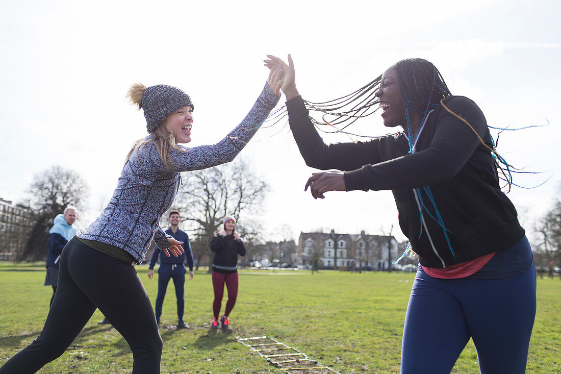 Enthusiastic women high-fiving, exercising in sunny park