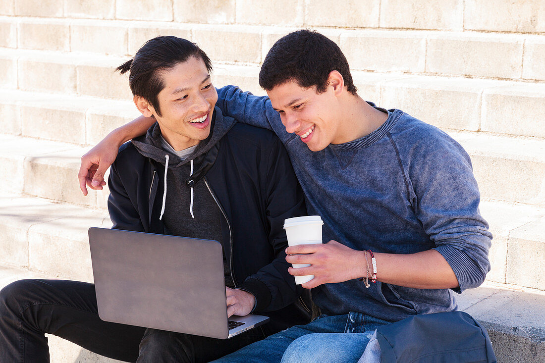 Male gay couple using laptop and drinking coffee