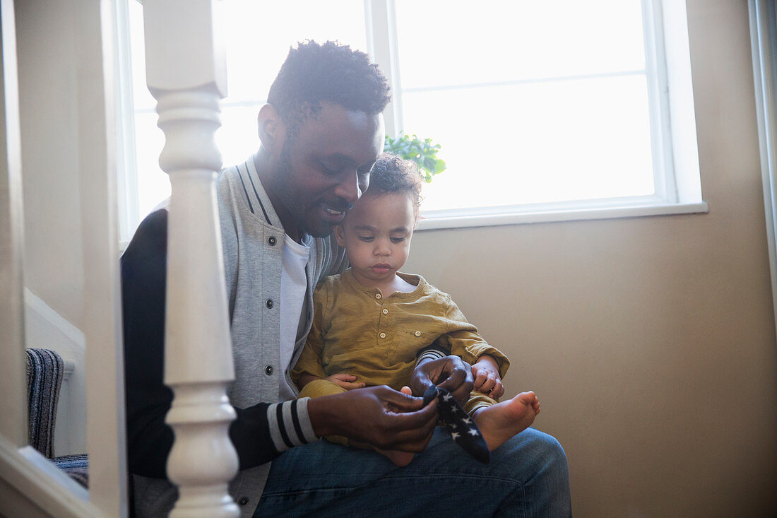 Father putting socks on baby son on stairs