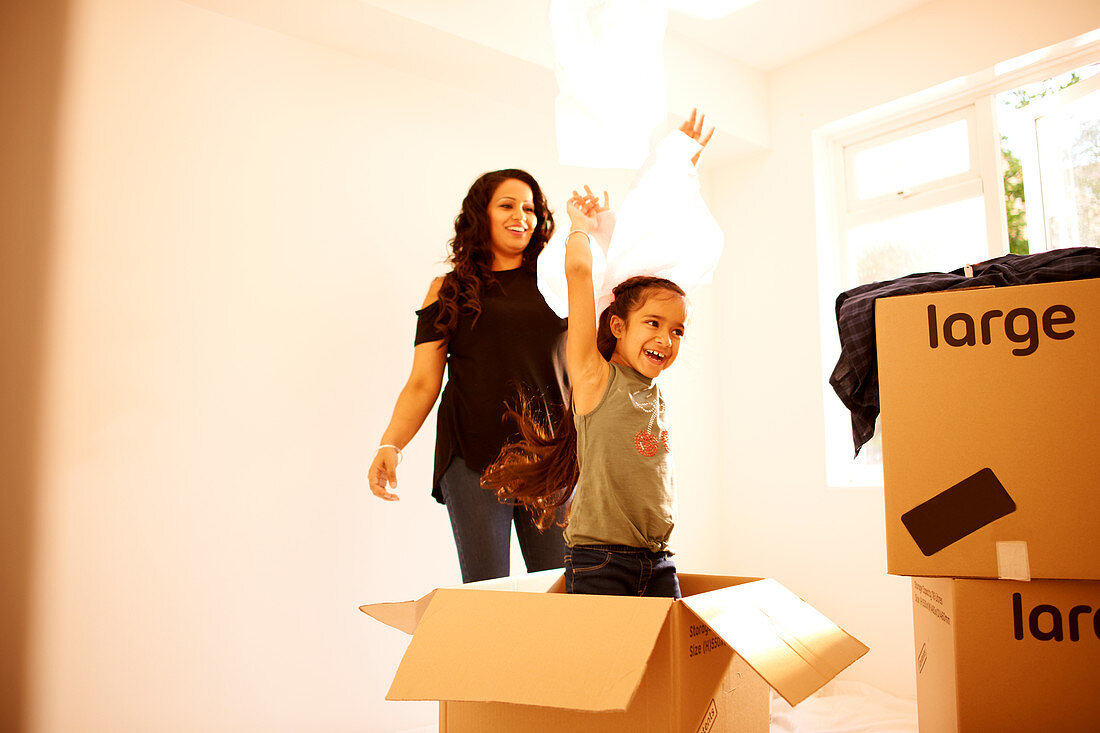 Playful mother and daughter moving into new home