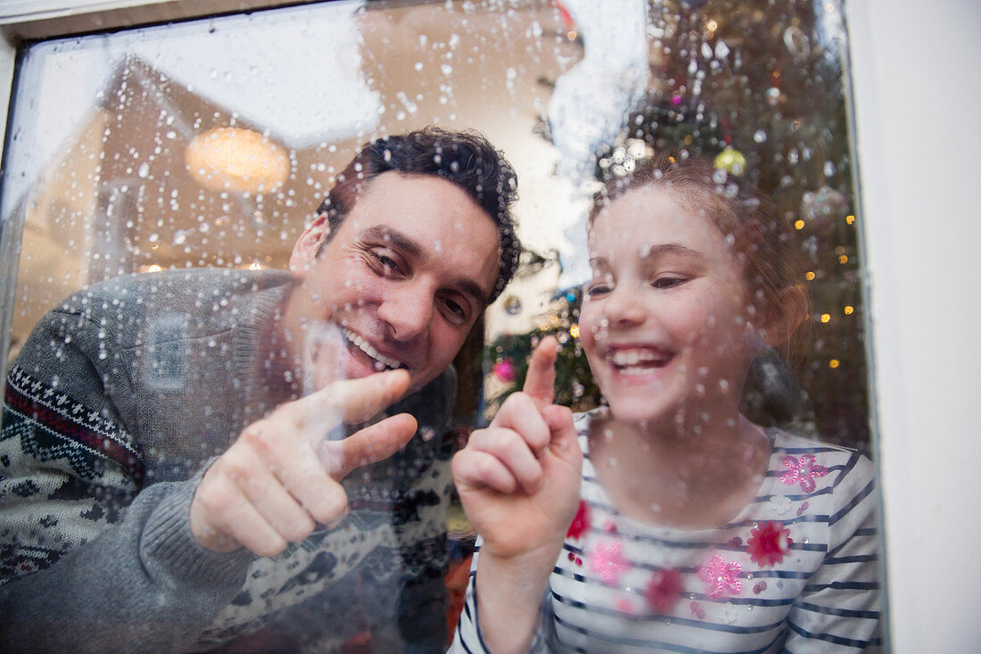 Father and daughter drawing on wet winter window