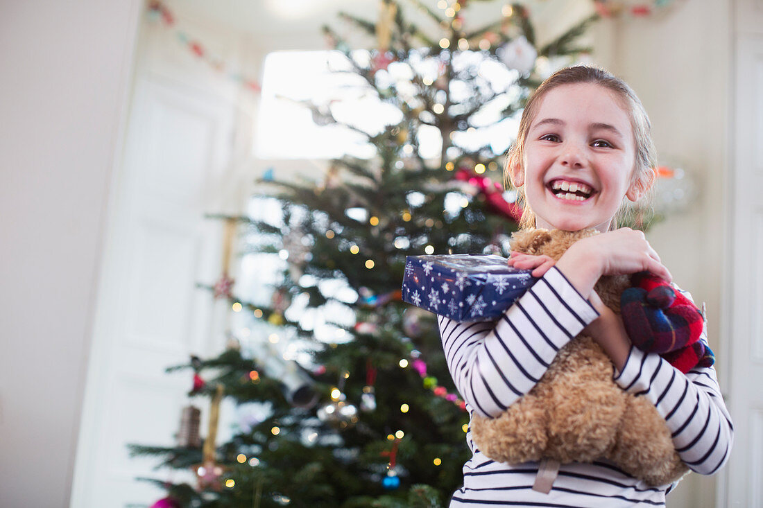 Girl hugging teddy bear in front of Christmas tree