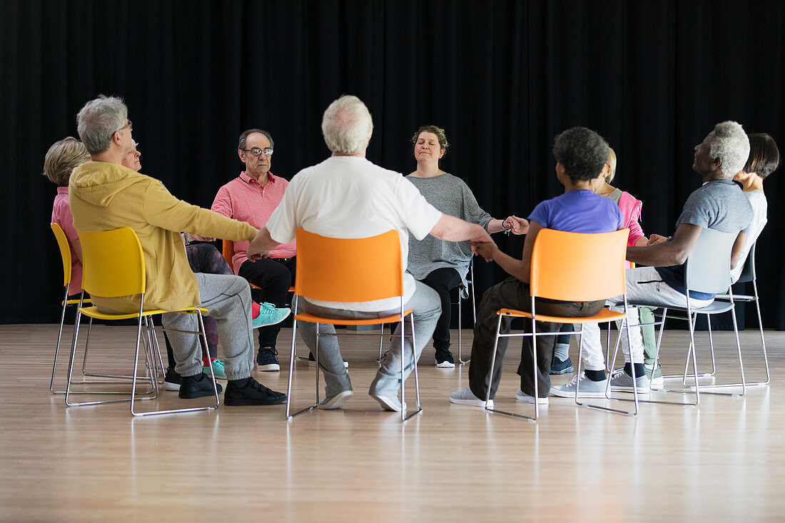 Active seniors meditating, holding hands in circle