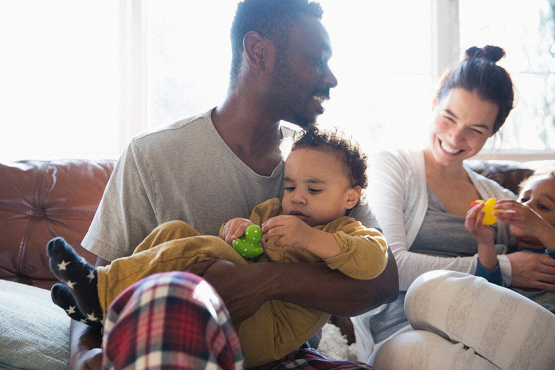 Multi-ethnic family in pyjamas cuddling on sofa