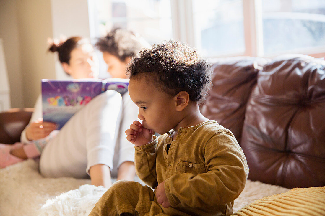 Innocent baby boy sucking thumb on sofa